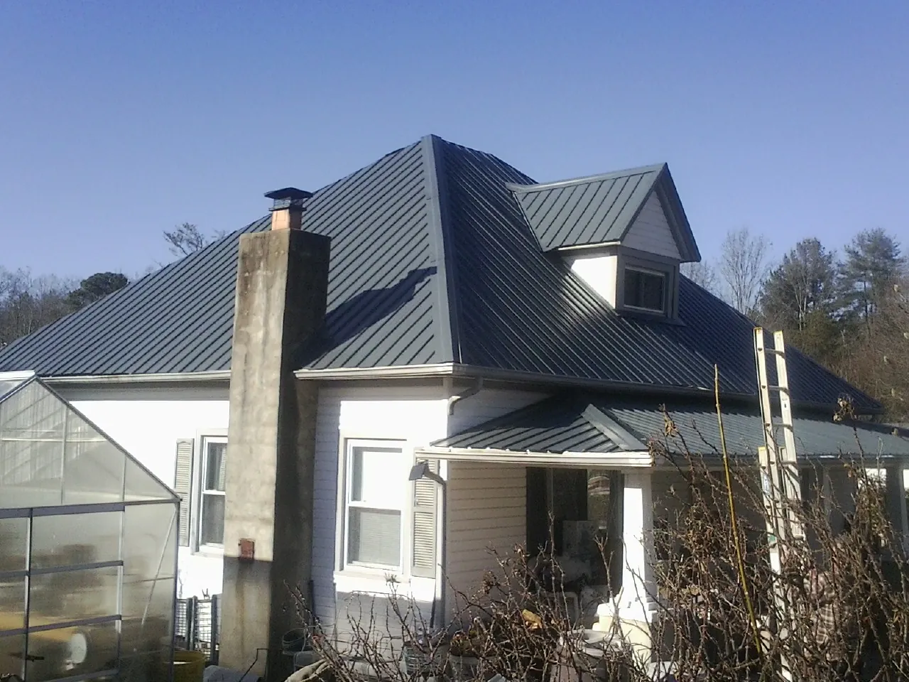 Dark blue standing seam metal roof on a white farmhouse with dormer — Slate & Tile Roof Repair by Roofing Brothers in Speonk