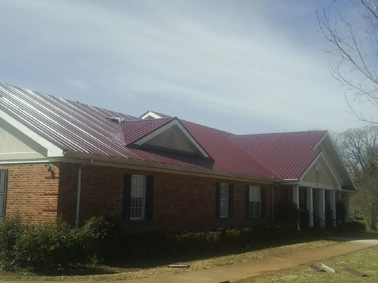 Red metal roof with gabled entries on a long brick building, from a Hail Damage Roof Repair job in Speonk