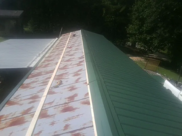 Old rusted panels beside newly installed green metal roofing — Wind Damage Roof Repair by Roofing Brothers in Speonk