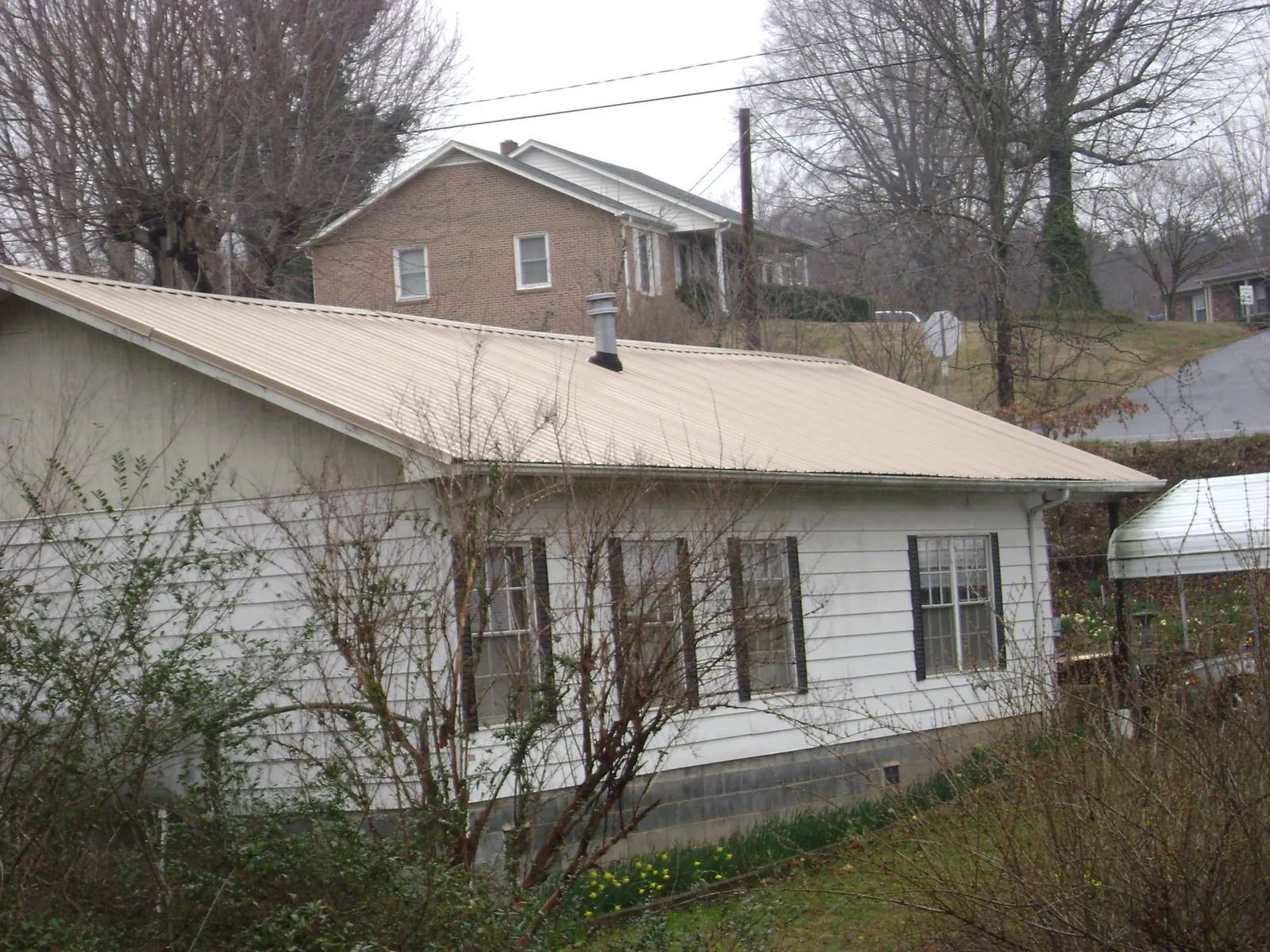 Tan metal roof on a white sided house set into a hillside — Commercial Roofing by Roofing Brothers in Speonk